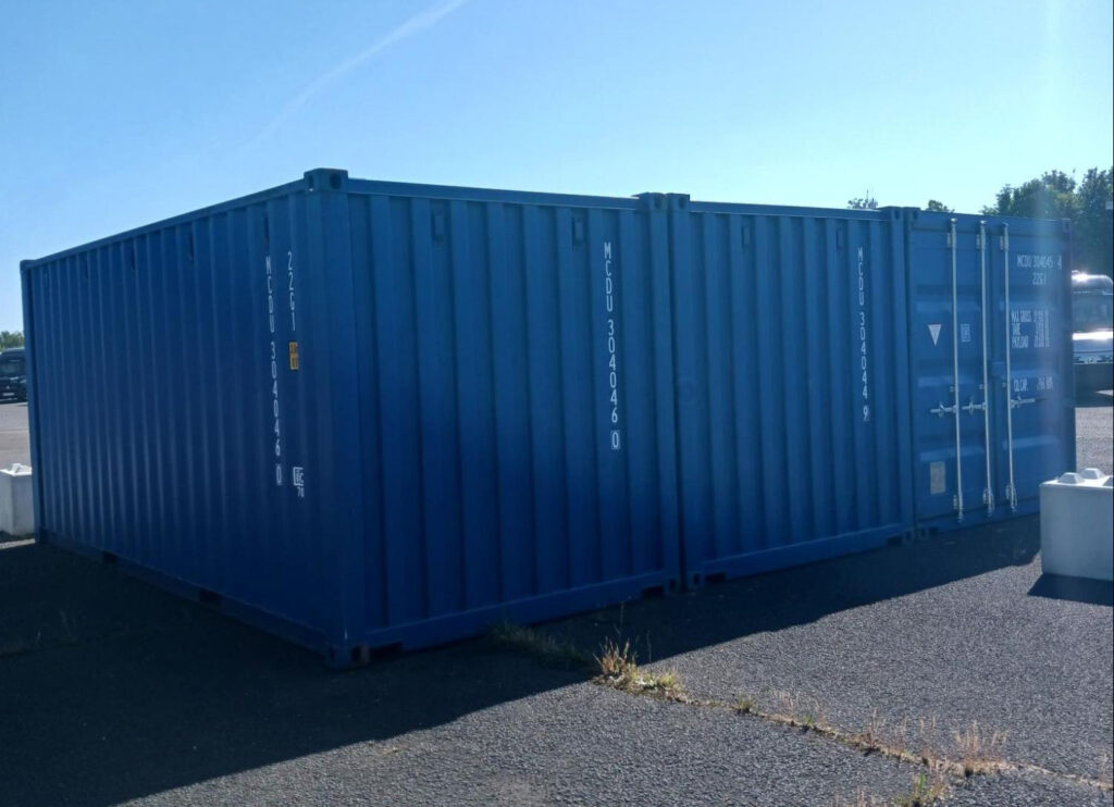 Trois containers maritimes bleus de stockage alignés sur aire stabilisée